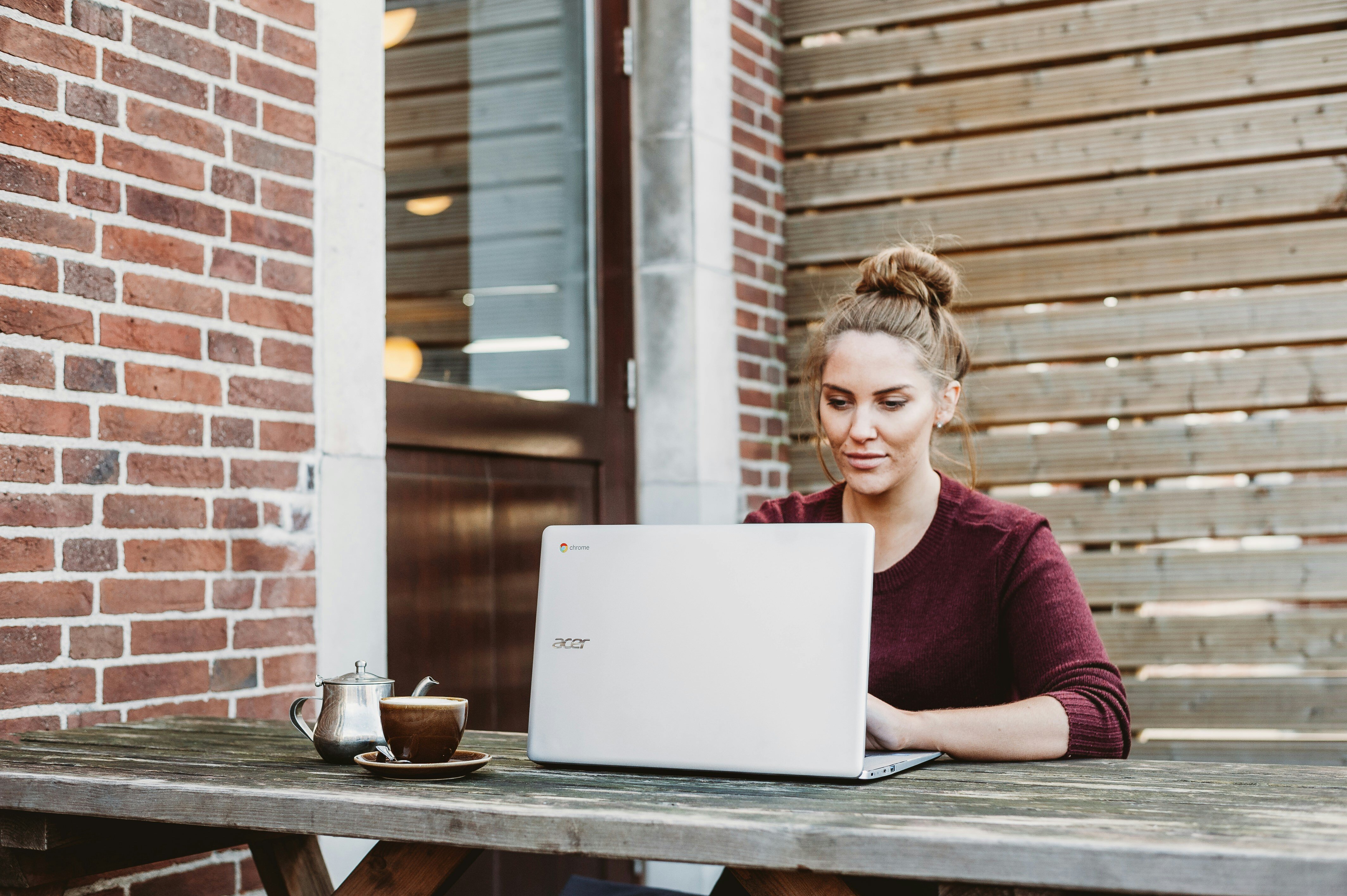 Blonde Frau sitzt draussen am Laptop bei schönem Wetter