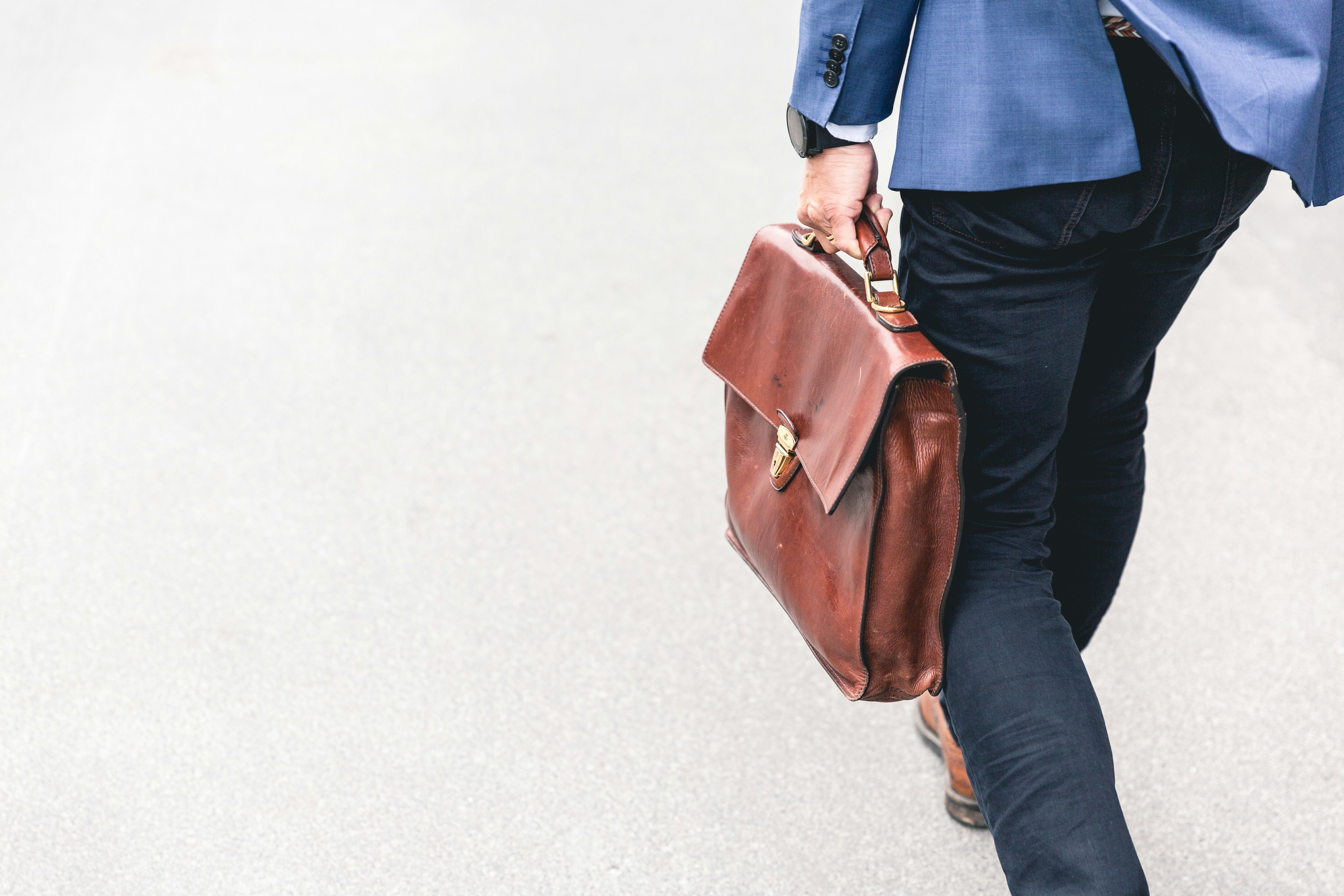 Einen Man im Anzug trägt eine Laptoptasche aus leder in der linken Hand