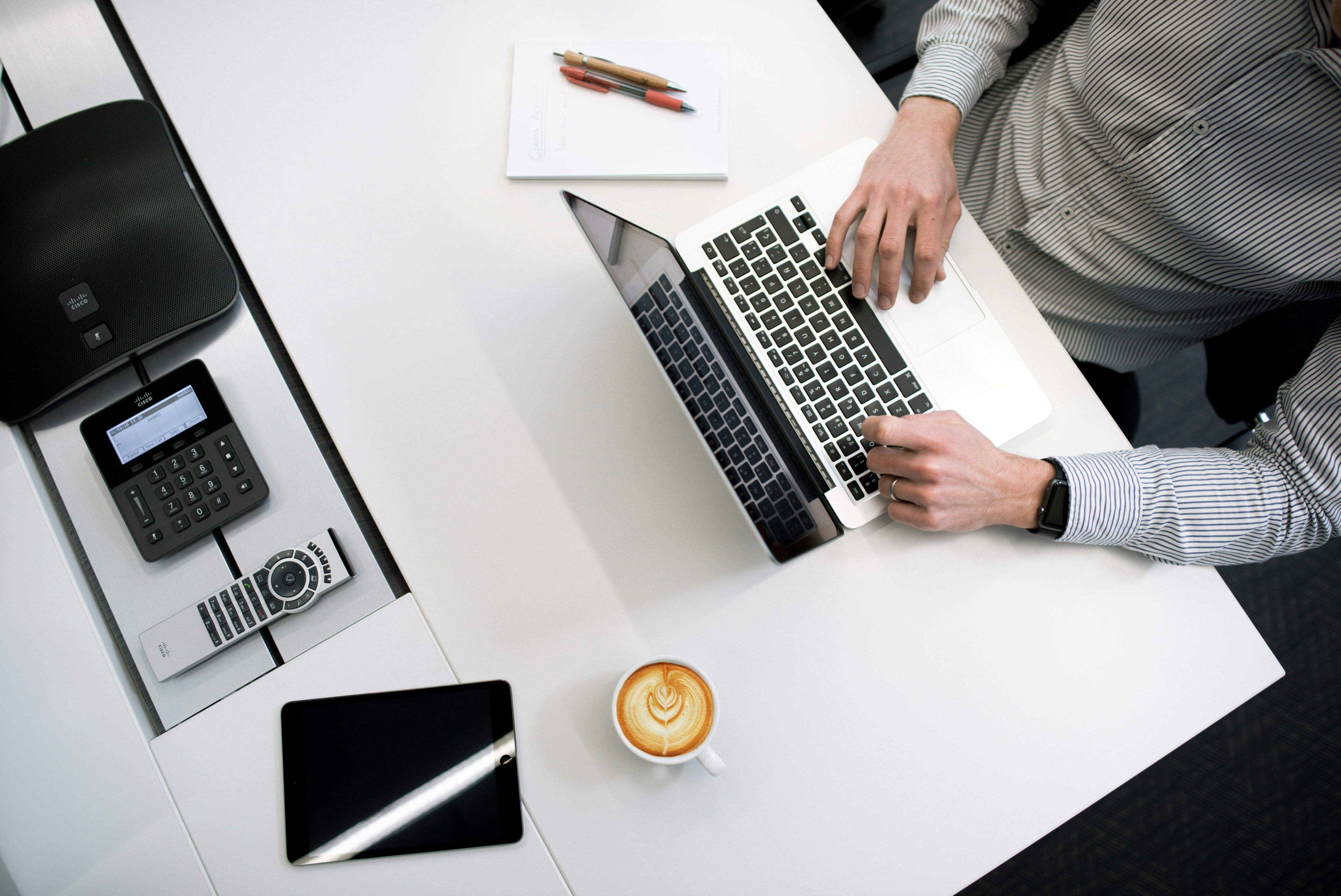 Junger man sitzt an einem Schreibtisch mit Laptop, Kaffe, Tablet und Notizblock
